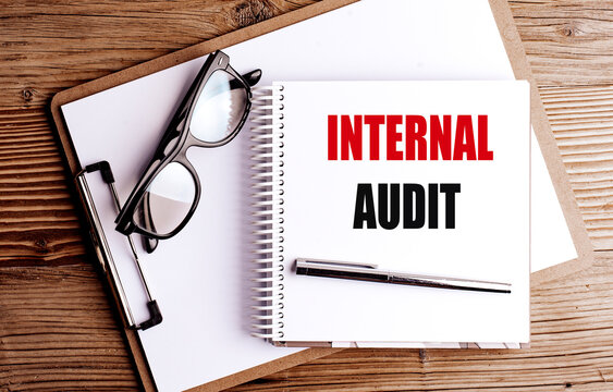 Internal audit concept with notebook clipboard eyeglasses and pen on wooden desk representing corporate compliance