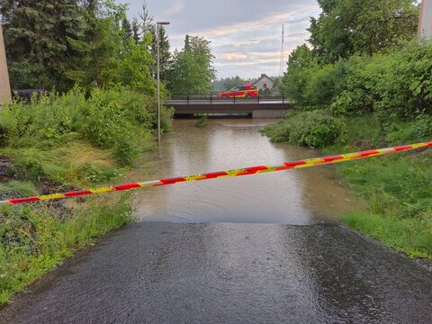 Red fire engine driving over a bridge above a heavily flooded pedestrian path after a summer storm