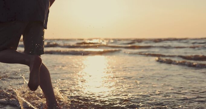 Child running barefoot on the beach at sunset, water is splashing. Carefree childhood. slow motion