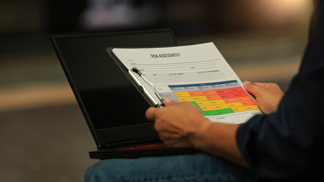 Focused professional hand holds business continuity risk planning document on clipboard near laptop computer with serious concentration