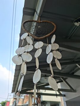 heart-shaped dreamcatcher wind chime featuring white translucent capiz shells hanging down in multiple vertical rows under an outdoor roof.