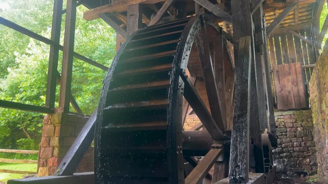 Large antique colonial American hydro power water wheel turns as water spills from sluice Green nature background copy space innovation early American history Pennsylvania industry renewable resource