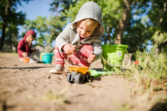 Toddler boy in hoodie plays with truck outside
