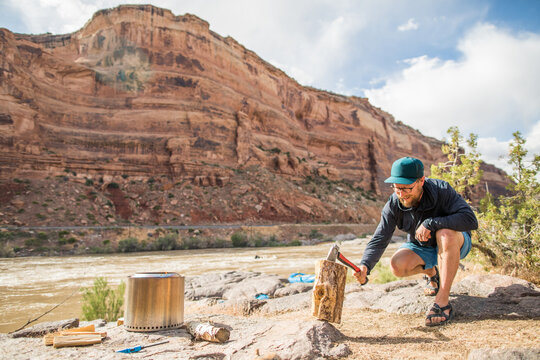 A man splits a log with a hatchet while camping