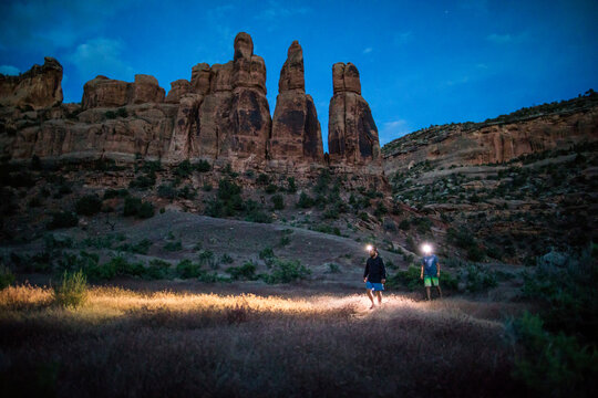 Two adventurous men hiking with headlamps below dessert rock formation
