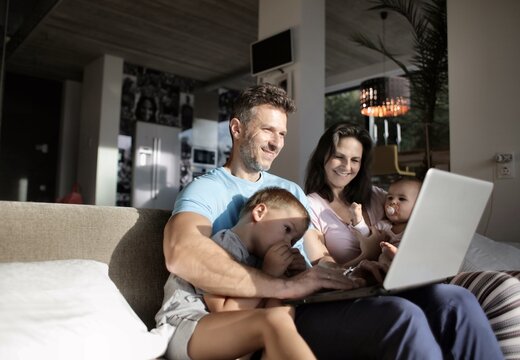 Happy family of four using laptop computer on sofa