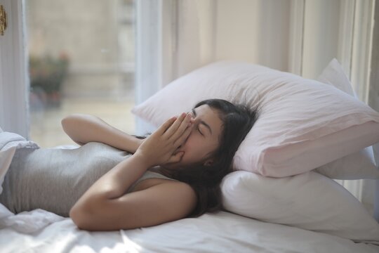 Sleepy young woman waking up and rubbing her eyes in bed