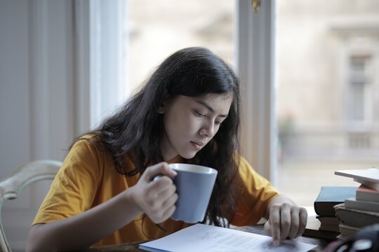 Young woman studying papers while holding mug