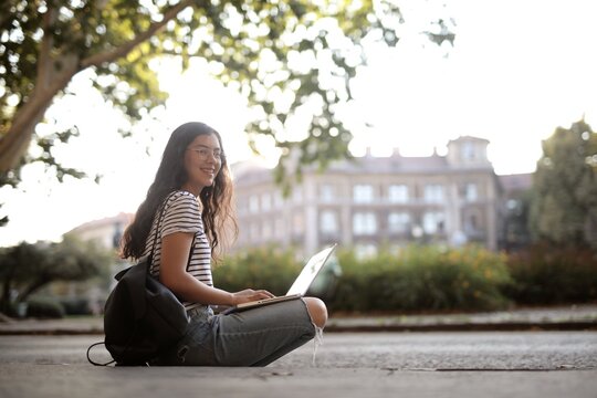 Happy student sitting outdoors using her laptop