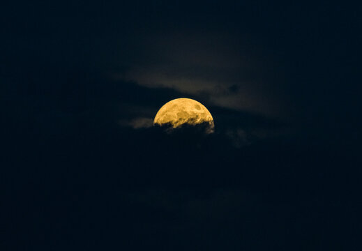 Glowing yellow full moon shining bright through night sky clouds
