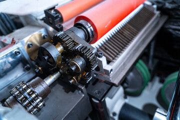 Fototapeta premium Close-up view of a complex industrial machine with metal gears, chain, and red rollers