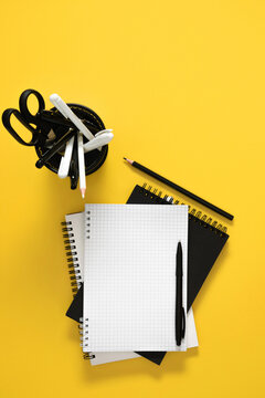 Vertical Flat Lay with Blank Grid Notebook, Black Pen, and Stationery Organizer on Bright Yellow Background. Contrast Minimalist Office and Back to School Concept Layout. Top View.