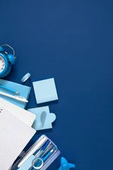 Vertical Blue Stationery Flat Lay with Blank Grid Notebook, Alarm Clock, Pencil Case, and Sticky Notes on Dark Blue Background. Back to School, Office, and Education Concept with Ample Copy Space. © prime1001