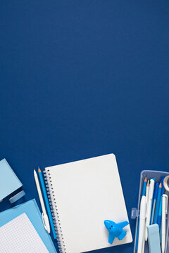 Vertical Blue Stationery Flat Lay with Open Blank Notebook, Pencil Case, Pencil, and Sharpener Airplane on Dark Blue Background. Back to School and Business Concept with Copyspace on Top. Top View.