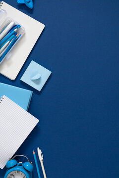 Vertical Blue Stationery Flat Lay with Notebooks, Pencil Case, Alarm Clock, and Heart Note on Dark Blue Background. Back to School, Office, and Education Concept with Ample Right Side Copy Space.