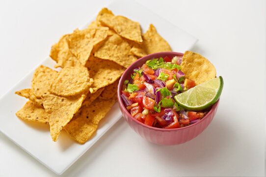 Pico de gallo bowl with a tortilla chips on the side on a white background. Side view