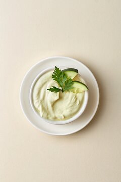 Creamy hummus dip bowl with cucumber slices and parsley garnish on a beige background. Top view, negative space