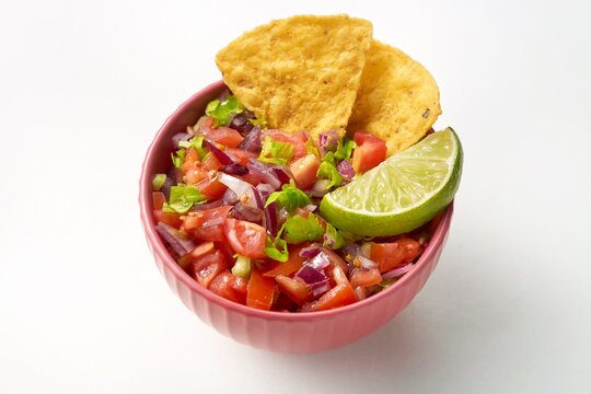 Pico de gallo bowl with a tortilla chips on the side on a white background. Side view