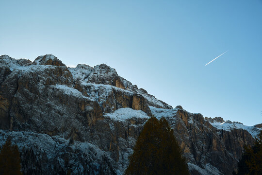 Plane with chemtrail flying across rocky snow mountains - Dolomites Italy 