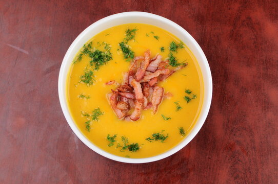 Creamy Pumpkin Soup with Bacon and Dill in Bowl on Wooden Table