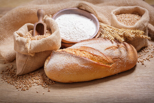 fresh bread, bowl of flour, wheat grains and spikelets on wooden table