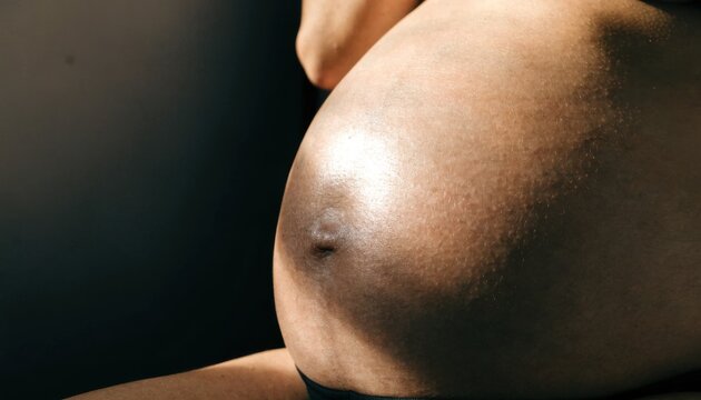 Pregnancy body strength concept. Close-up image of a pregnant belly with a prominent navel and smooth skin under warm lighting.