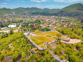 Obraz premium Montenegro flag flying high on Orlov Krs, overlooking historical capital Cetinje town and surrounding green mountains