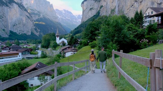 Switzerland welcomes you to Lauterbrunnen, where travelers stroll along a scenic path embraced by majestic peaks. Experience the tranquility and beauty of this enchanting valley destination.