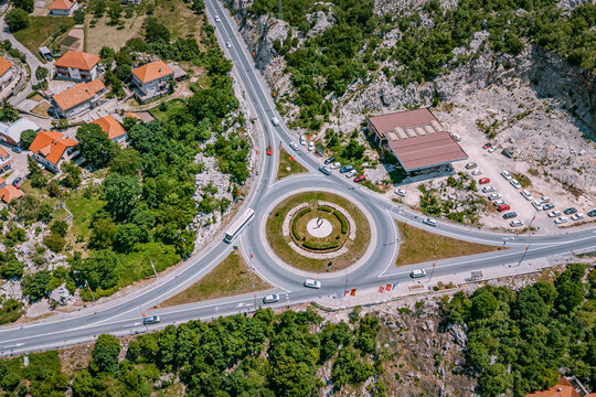 Vehicles navigating a busy roundabout and connecting roads, surrounded by lush green mountains and buildings near Cetinje, Montenegro
