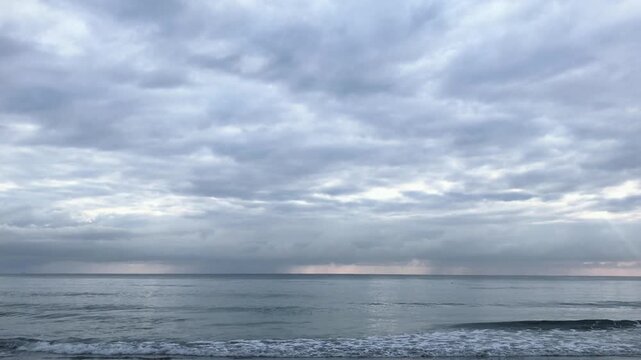 A serene and cinematic wide-angle shot of a calm ocean under a moody, overcast sky