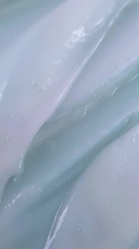 Top down view of stirring white cream with a tool. Vertical close up of beauty cream being stirred and spreading outward. Skincare preparation concept.