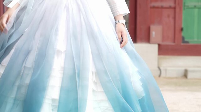 Soft blue and white gown flows with grace. Person moves gently, creating a dreamy, ethereal effect. Traditional architecture frames the scene with warmth. Ideal for fantasy, romance