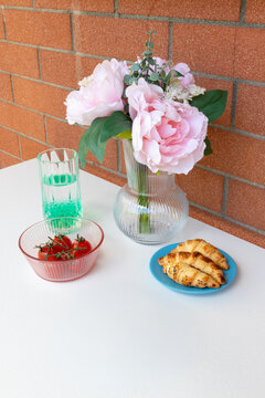 Elegant floral and breakfast still life with peonies, strawberries and croissants
