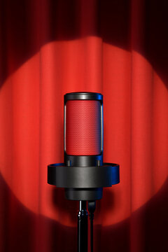 Black microphone glowing red light with spotlight on red stage curtain.
