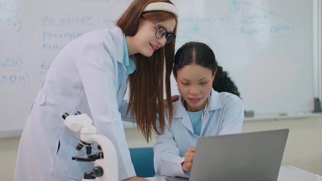 Two medical students collaborating to prepare an anatomy lesson using a laptop in a classroom equipped with a whiteboard and educational teaching materials.