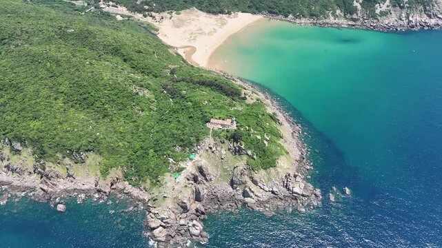 Drone footage orbiting above Bai Mon Beach and Mui Dien Lighthouse (Cape Dai Lighthouse) in Dak Lak (formerly Phu Yen) Province, Vietnam. From above, the natural arrangement of the sandy beach and roc
