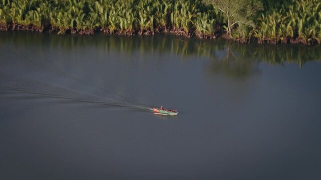 Small boat cruising along the Abatan River beside lush mangrove forest, aerial tracking sideview