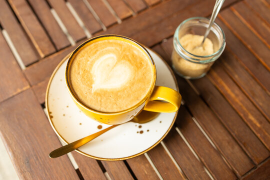 Yellow cup of cappuccino coffee with latte art on wooden table