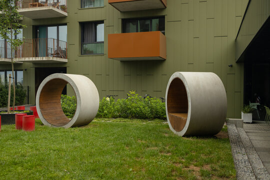 A beautifully landscaped courtyard of a modern apartment complex featuring unique concrete pipes or tunnels for children on a green lawn.