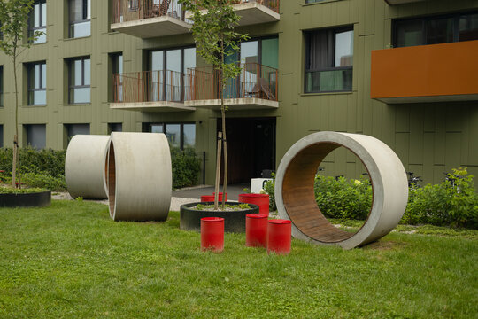 A beautifully landscaped courtyard of a modern apartment complex featuring unique concrete pipes or tunnels for children on a green lawn.