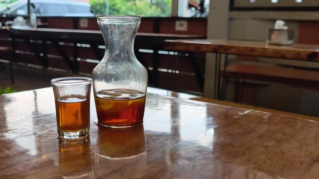 Wide vertical shot of cold brew iced coffee on a rustic wooden table with a blurred background of a cozy modern coffee shop interior.