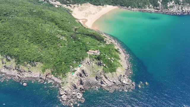 Drone footage orbiting above Bai Mon Beach and Mui Dien Lighthouse (Cape Dai Lighthouse) in Dak Lak (formerly Phu Yen) Province, Vietnam. From above, the natural arrangement of the sandy beach and roc