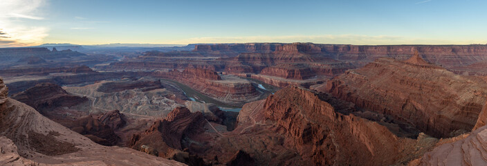 Naklejka premium Majestic breathtaking canyon landscape features deep valley winding river red rock formations under vast bright sky creating awe inspiring scenic view across dry desert terrain of utah usa