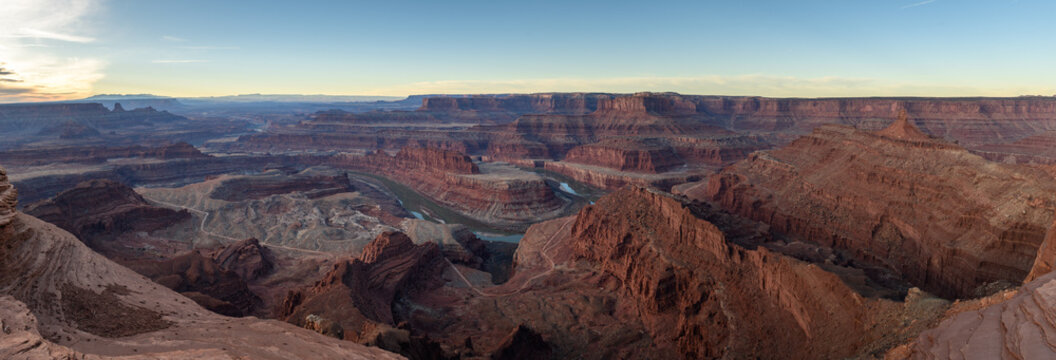 Majestic breathtaking canyon landscape features deep valley winding river red rock formations under vast bright sky creating awe inspiring scenic view across dry desert terrain of utah usa