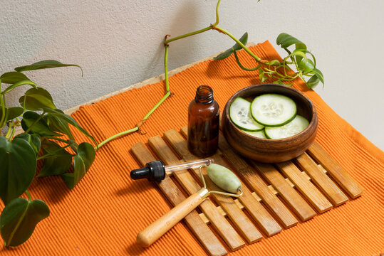 Top view of facial serum, facial massager, skincare products, and cucumber slices in a bowl on a table. Concept of spa, beauty, and self care