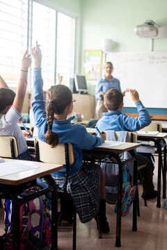 Elementary school students raising their hands during a classroom lesson