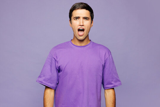 Young sad shocked surprised astonished Caucasian man he wear violet t-shirt casual clothes look camera with opened mouth isolated on plain pastel purple background studio portrait. Lifestyle concept.