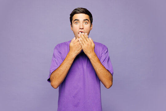 Young sad shocked surprised Caucasian man he wear violet t-shirt casual clothes cover mouth with hand look camera isolated on plain pastel light purple background studio portrait. Lifestyle concept.