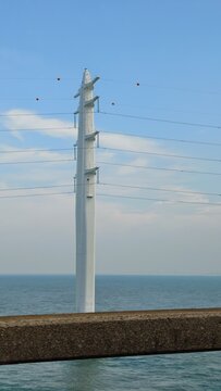 White monopole electricity pylon standing in the ocean under a blue sky.