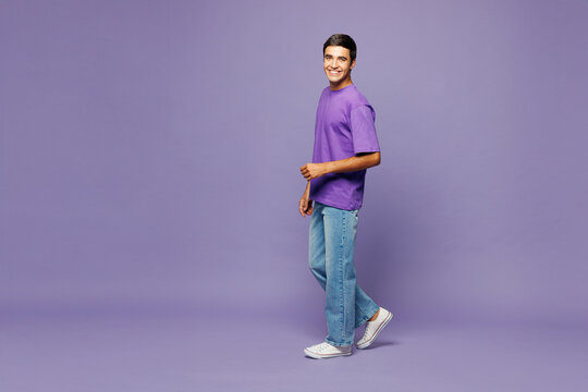Full body side view smiling happy young Caucasian man wear violet t-shirt casual clothes walking going look camera isolated on plain pastel light purple background studio portrait. Lifestyle concept.